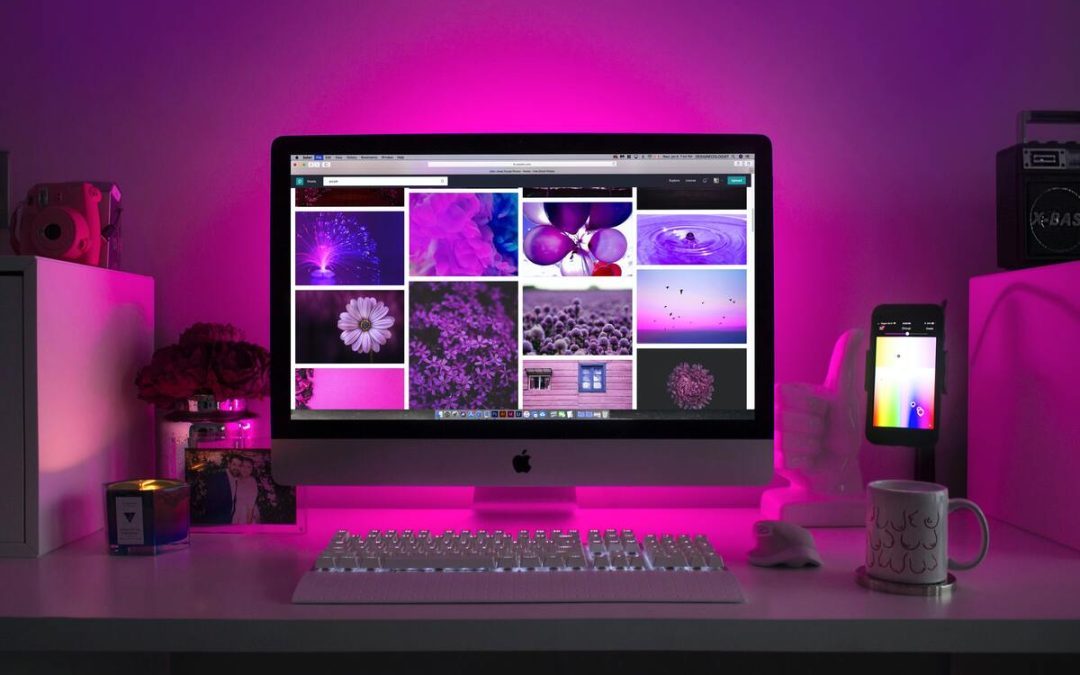 Vibrant workspace with an Apple iMac surrounded by purple LED lights and creative desk decorations