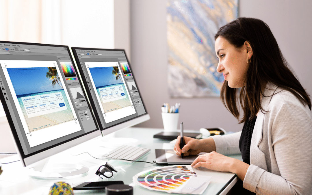 Female web designer working on a beach-themed website on dual monitors in a modern office.