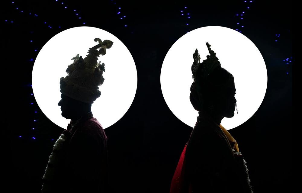 Traditional couple silhouetted against bright circular lights in a cultural event.