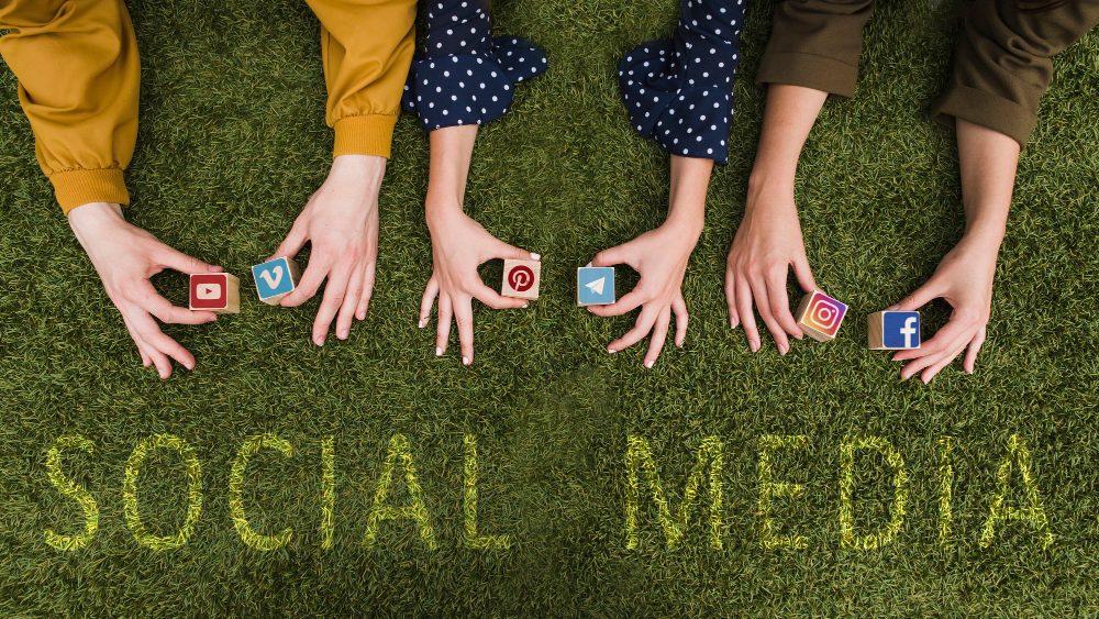 Hands holding social media icons over grass with the words “Social Media.”