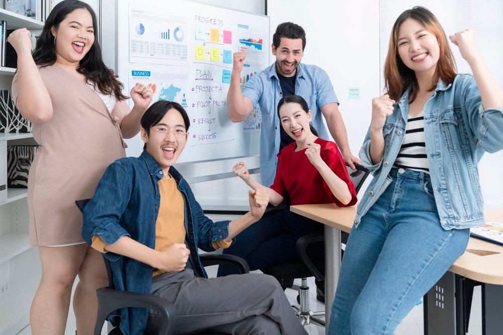 Happy team of diverse employees cheering with fists raised in a modern office