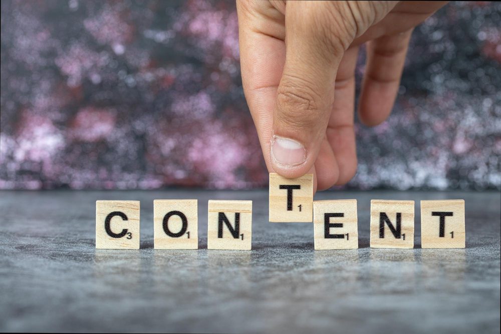 Hand arranging Scrabble tiles spelling 'CONTENT' on a textured surface with a blurred background.