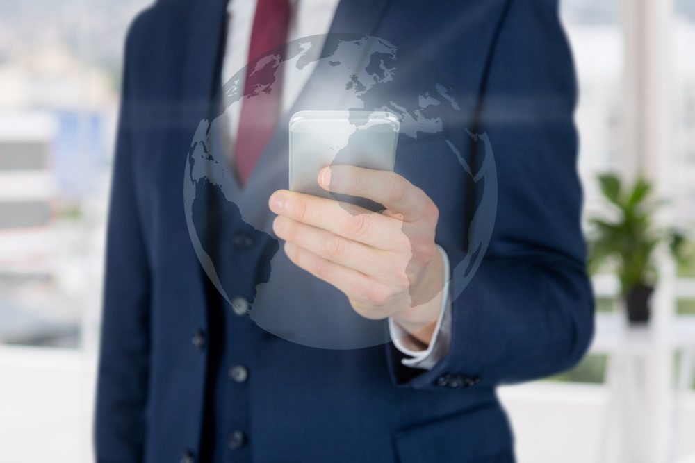 Businessman in a suit using smartphone with a transparent globe overlay in a modern office