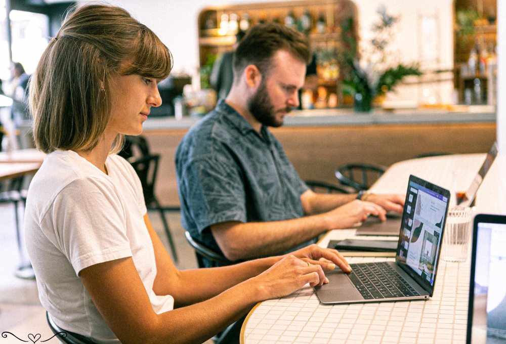 Two people working on laptops at a cozy café, focused and productive.