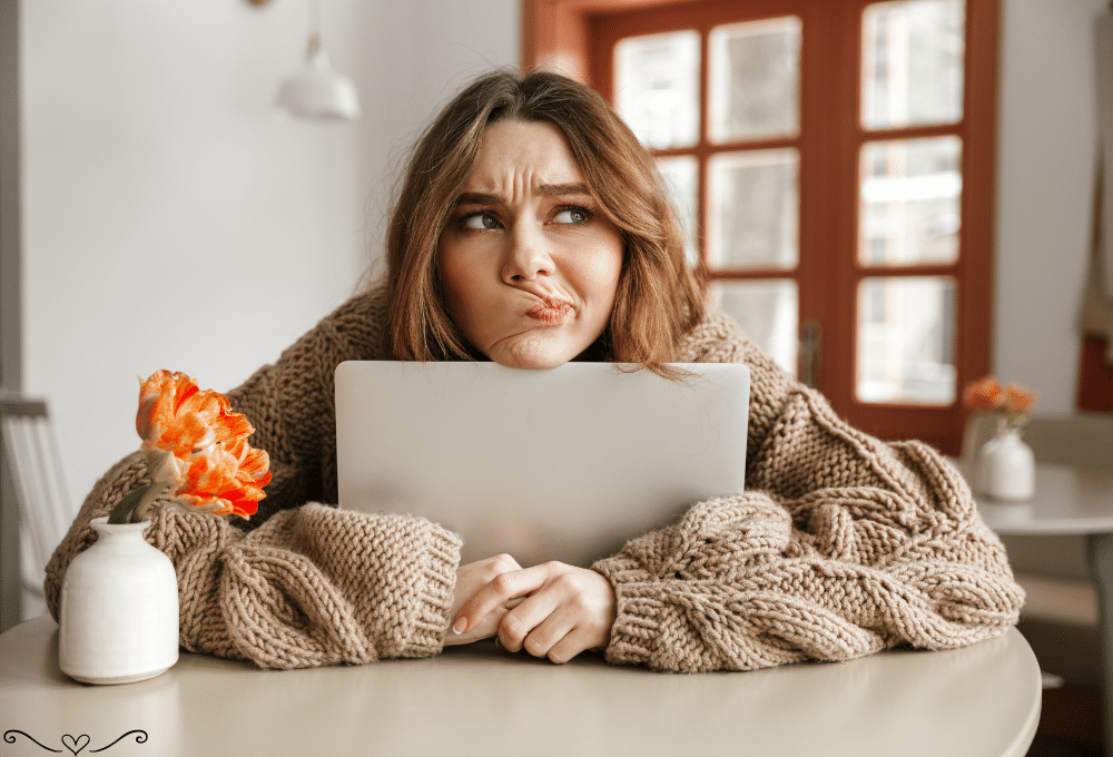 Woman in a cozy beige sweater holding a laptop, sitting at a table with orange flowers in a vase