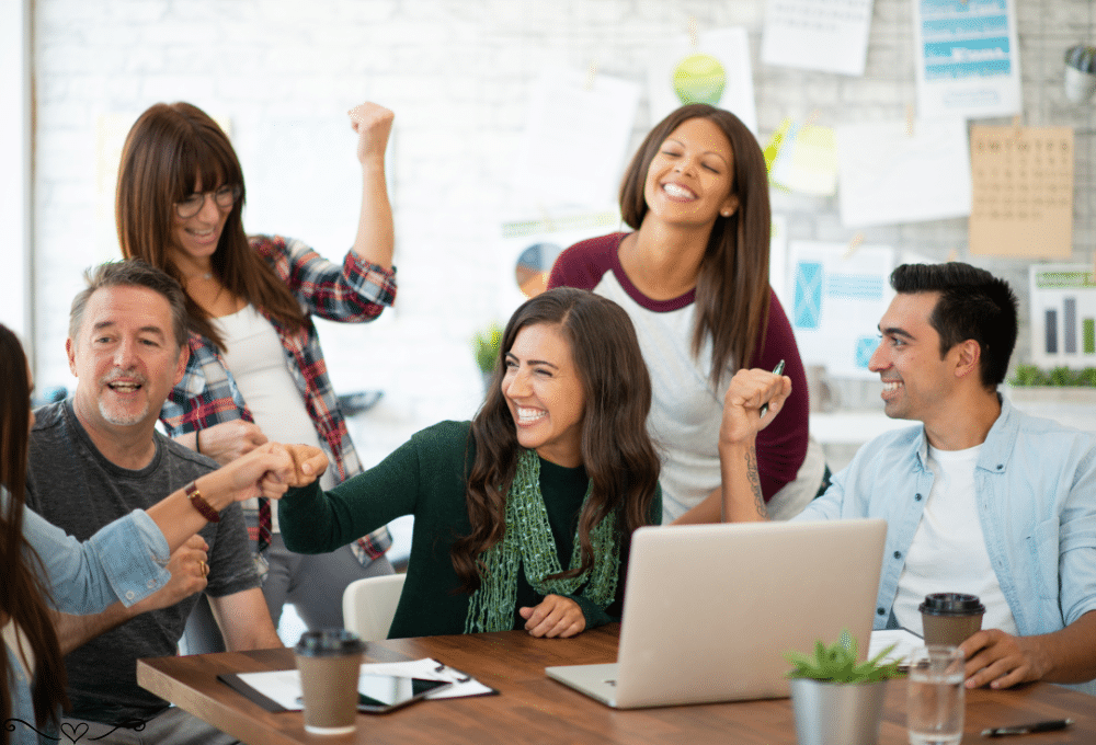 Diverse coworkers in a lively office celebrate a team success with fist bumps and smiles.