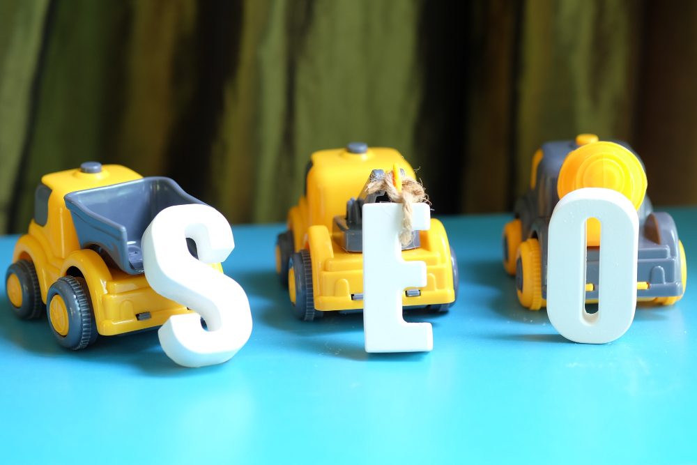 Yellow toy trucks forming SEO with white letters on a blue surface.