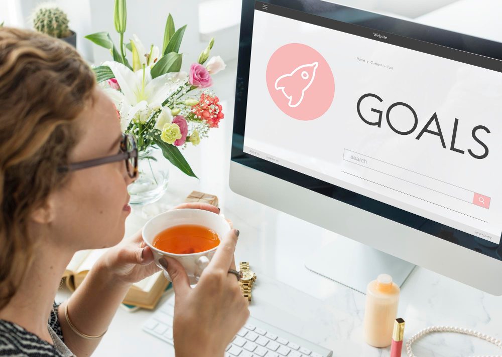 Woman sipping tea while planning goals with an inspiring desktop setup.