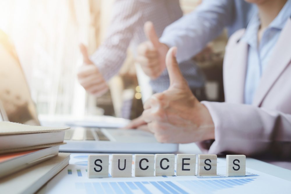 Thumbs up for success with letter blocks on a desk in a bright office setting.