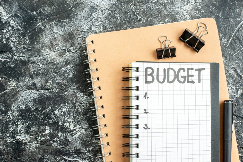 Budget planning notebook with checkered pages and binder clips on a textured background.