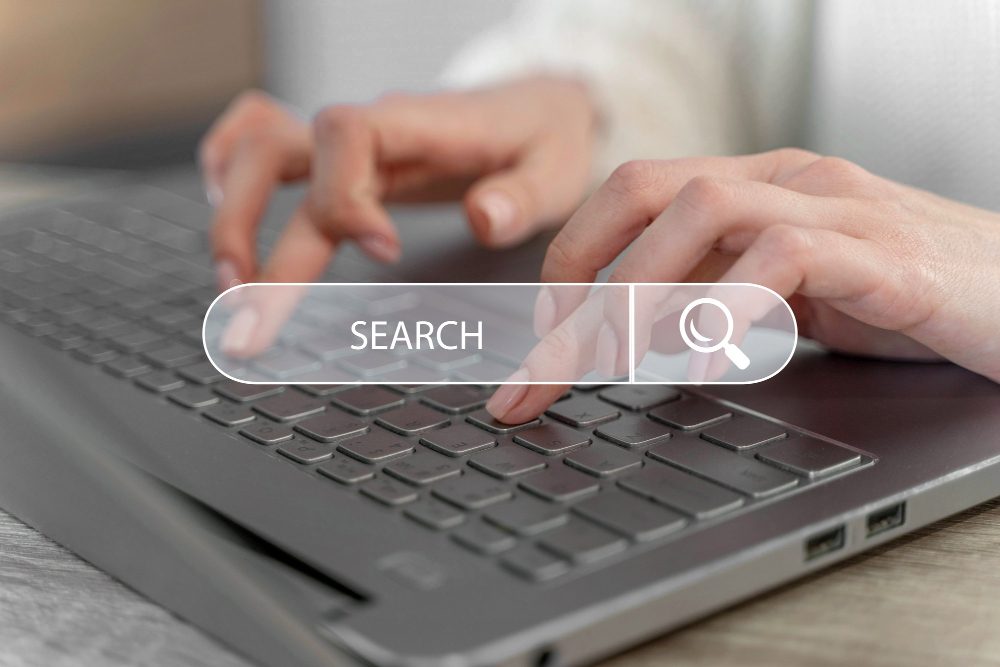 Hands typing on a laptop keyboard with a search bar overlay.