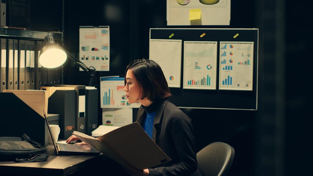 Focused woman working late in an office with charts in the background