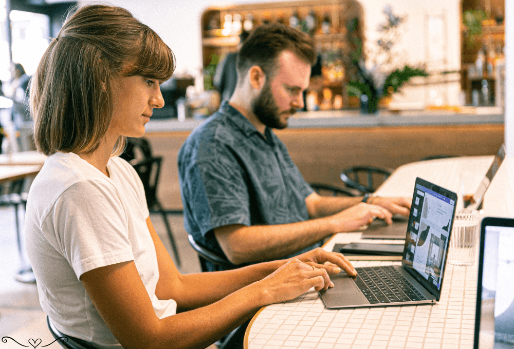 Two people working on laptops at a cozy café, focused and productive.