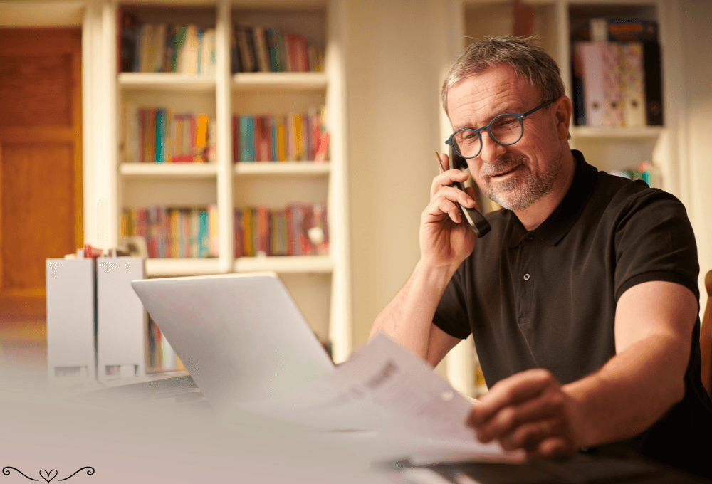 Man in black polo working on a laptop while talking on the phone